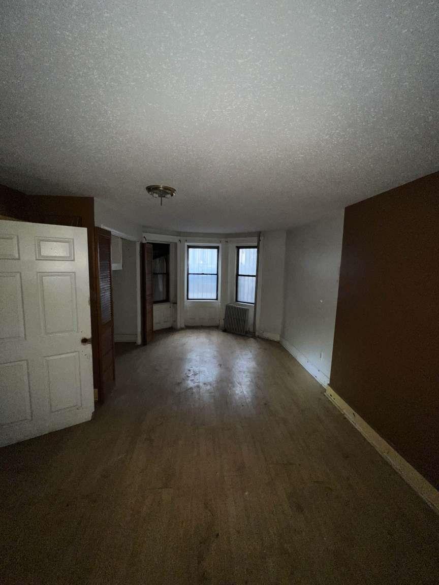 1430 Pacific Street Brooklyn, NY 11216 - Photo 6 of 24 Unfurnished room featuring hardwood / wood-style floors, radiator heating unit, and a textured ceiling