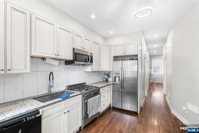 a kitchen with granite countertop a refrigerator a sink dishwasher a stove and white cabinets with wooden floor