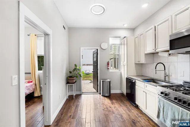 a kitchen with stainless steel appliances a stove top oven a refrigerator a sink dishwasher and white cabinets with wooden floor