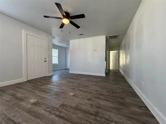 a view of an empty room with wooden floor and a ceiling fan