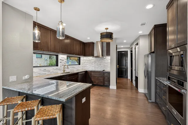 a large kitchen with stainless steel appliances kitchen island granite countertop a table chairs in it and wooden floors