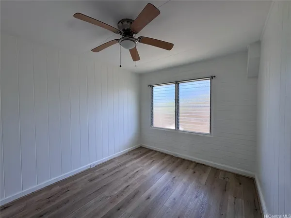 an empty room with wooden floor fan and windows