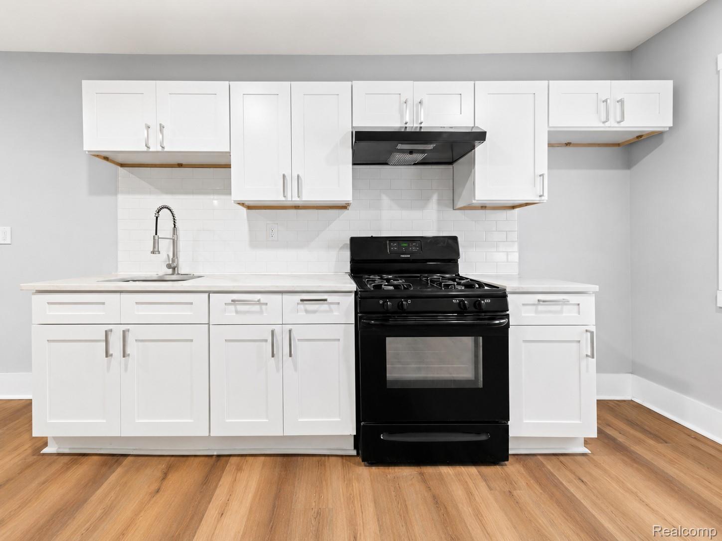 9175 Devonshire Road Detroit, MI 48224 - Photo 9 of 23 Kitchen featuring white shaker cabinetry, light-toned countertops, a full suite of black appliances, subway tile backsplash, and wood-finish flooring