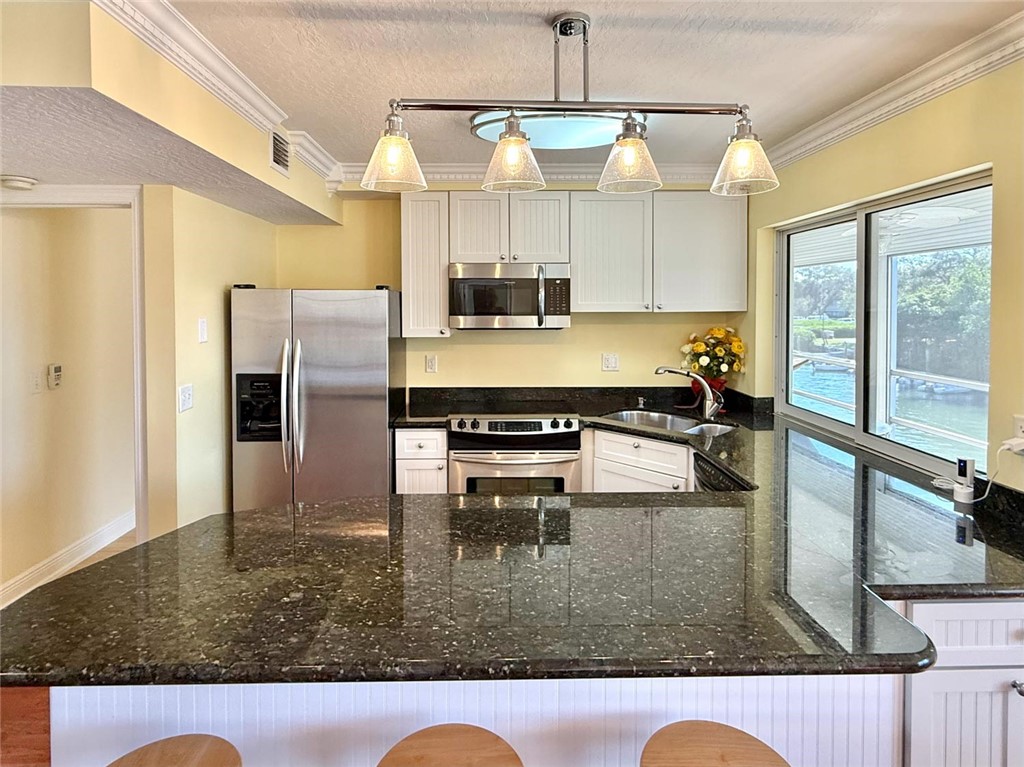 200 Greytwig Road, Unit 212 Vero Beach, FL 32963 - Photo 18 of 30 a kitchen with kitchen island granite countertop a refrigerator a stove and white cabinets with wooden floor