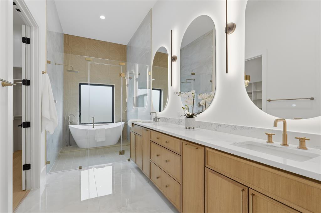 6038 Prospect Avenue Dallas, TX 75206 - Photo 19 of 40 Contemporary bathroom featuring a freestanding tub, glass-enclosed shower, dual vanities with white countertops, and illuminated oval mirrors