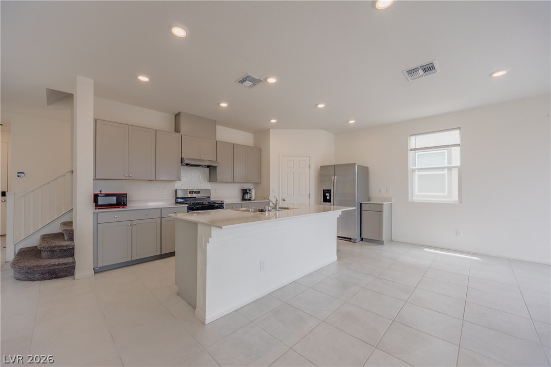 5927 Coja Street Las Vegas, NV 89113 - Photo 12 of 32 Kitchen featuring stainless steel appliances, gray cabinetry, light countertops, under cabinet range hood, and a center island with sink