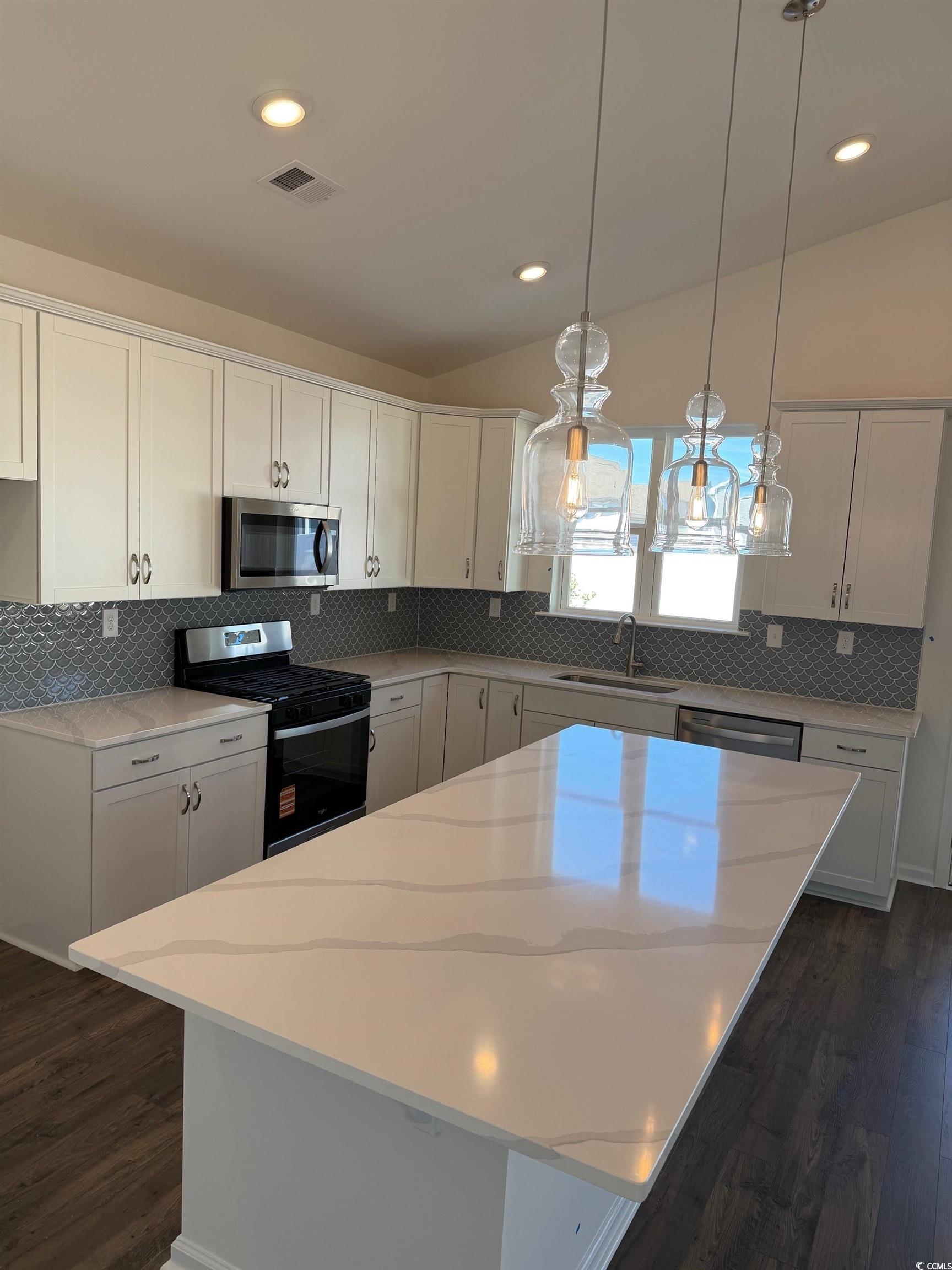 415 Kapalua Loop Little River, SC 29566 - Photo 5 of 19 Kitchen featuring appliances with stainless steel finishes, decorative backsplash, a center island with sink, light stone counters, and vaulted ceiling