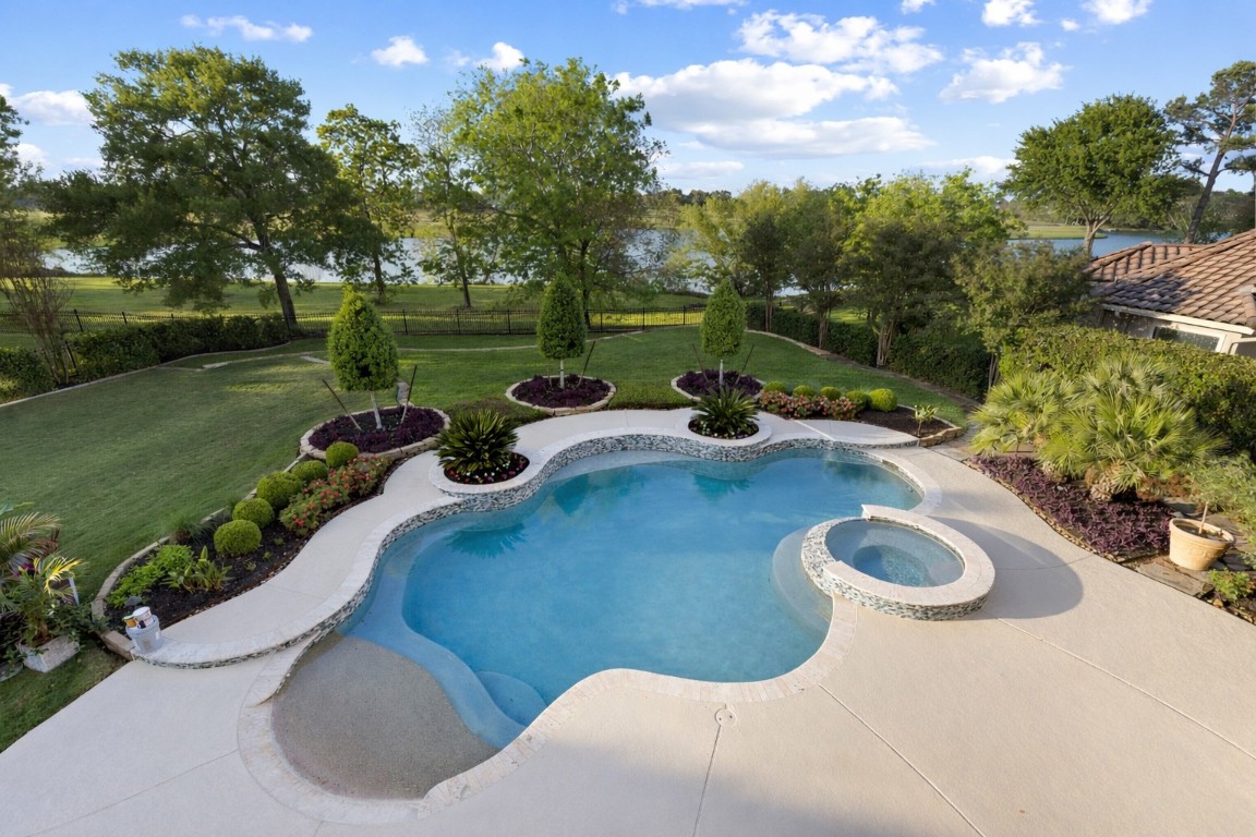 82 Manor Lake Estates Circle Spring, TX 77379 - Photo 4 of 50 The pool and raised spa create a striking focal point for the backyard, framed by lush landscaping and tranquil water views beyond. With updated equipment and a resurfaced finish, this outdoor centerpiece is designed for both relaxation and refined entertaining.
