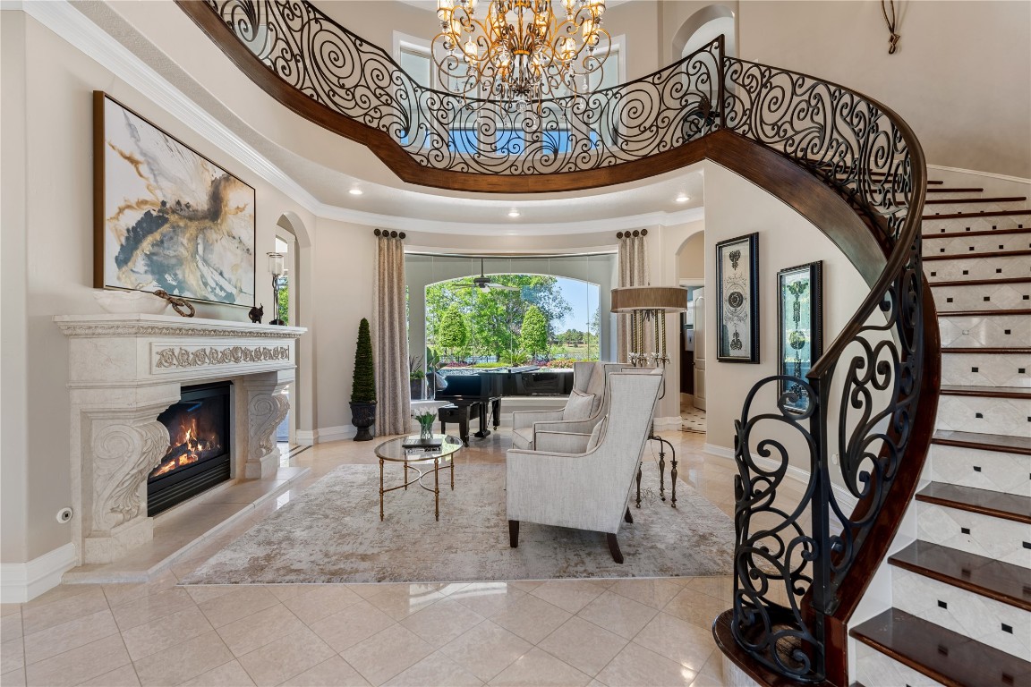 82 Manor Lake Estates Circle Spring, TX 77379 - Photo 6 of 50 The living room makes an unforgettable first impression with soaring ceilings, an ornate curved staircase, and a carved stone fireplace as its focal point. Natural light and garden views soften the scale, creating a room that is dramatic without feeling formal.