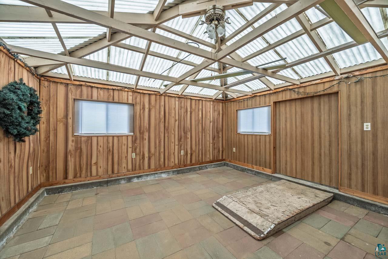 319 Michigan Avenue West Gilbert, MN 55741 - Photo 33 of 48 Enclosed patio room featuring a clear corrugated roof, exposed wood beam ceiling, wood plank wall paneling, two windows with blinds, and geometric tile flooring