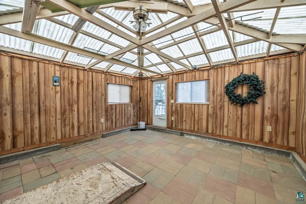 319 Michigan Avenue West Gilbert, MN 55741 - Photo 34 of 48 Enclosed patio featuring a translucent panel roof, exposed wood beam ceiling, wood-paneled walls, and multi-tone paver flooring