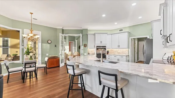 a kitchen with stainless steel appliances kitchen island granite countertop a dining table chairs and white cabinets next to a large window