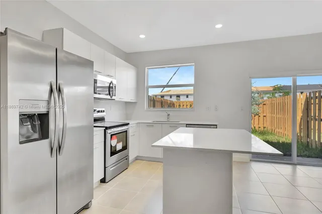 a kitchen with stainless steel appliances kitchen island granite countertop a refrigerator a stove and a sink with wooden floor