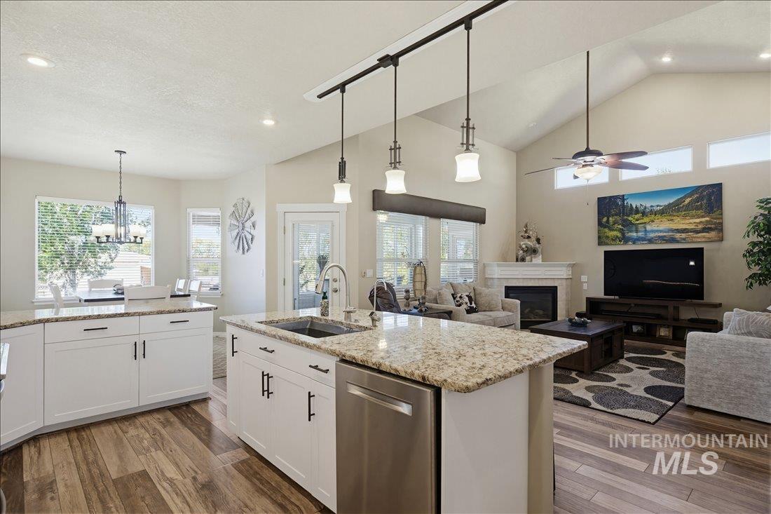 24623 Falcon Lane Caldwell, ID 83607 - Photo 11 of 40 Open-concept kitchen featuring an island with a stainless steel sink, granite countertops, white cabinetry with dark hardware, wood-finish flooring, and track lighting with pendant fixtures