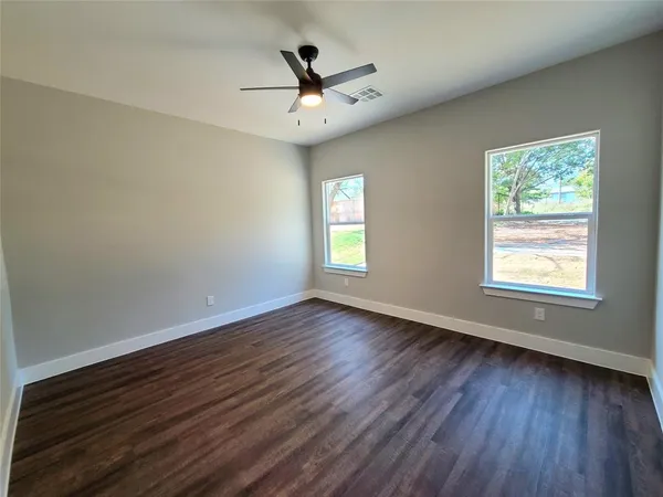 an empty room with wooden floor chandelier fan and windows
