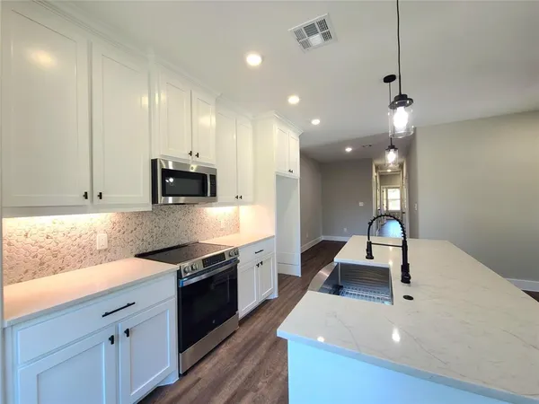 a kitchen with stainless steel appliances kitchen island granite countertop a sink a stove and a wooden floor