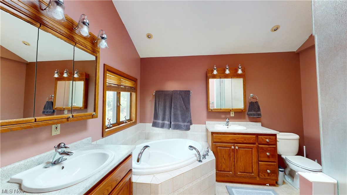 2980 Worrell Road Willoughby, OH 44094 - Photo 21 of 43 Primary Bathroom featuring dual vanity, vaulted ceiling, a relaxing tiled bath, toilet, and tile floors