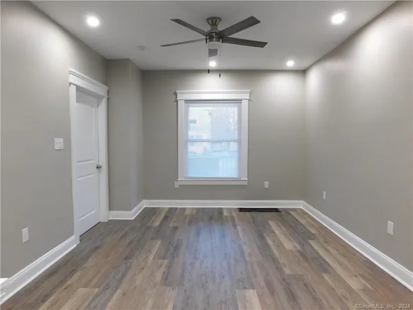 an empty room with wooden floor a ceiling fan and windows