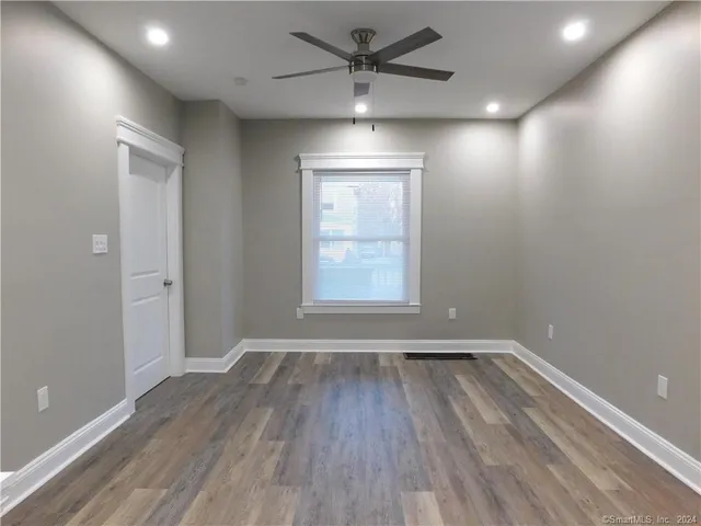 an empty room with wooden floor a ceiling fan and windows
