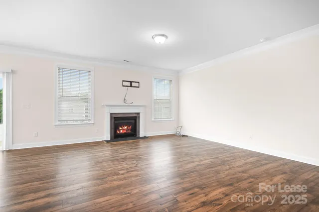 a view of an empty room with wooden floor fireplace and a window
