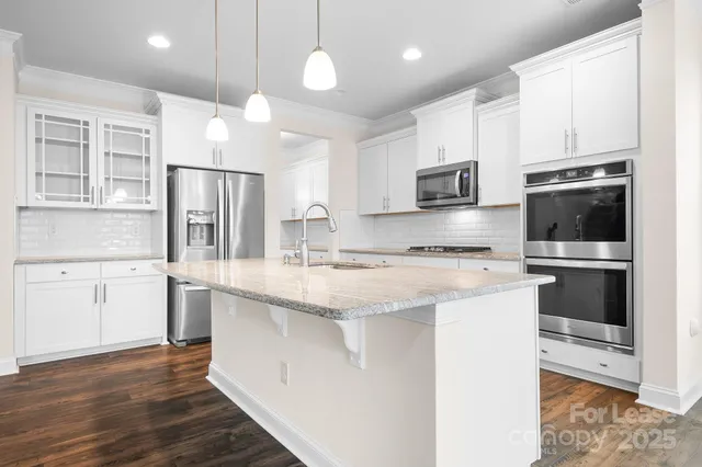 a kitchen with stainless steel appliances granite countertop a refrigerator a stove a sink and white cabinets with wooden floor