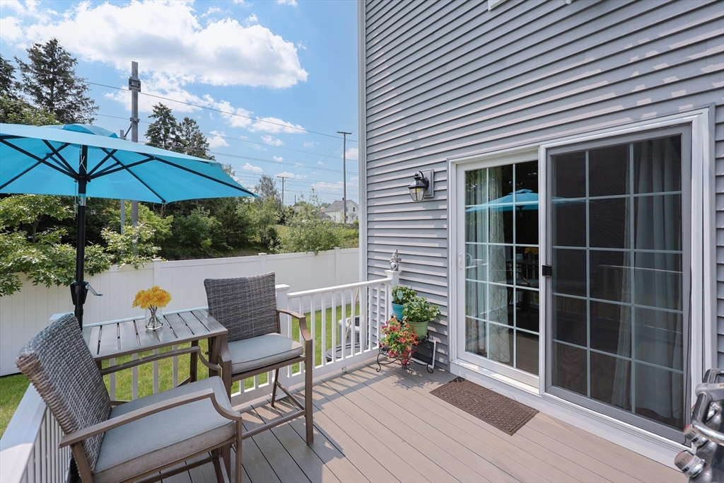 5 Mendon Road, Unit D Attleboro, MA 02703 - Photo 35 of 38 a view of a deck with table and chairs under an umbrella with wooden floor and fence