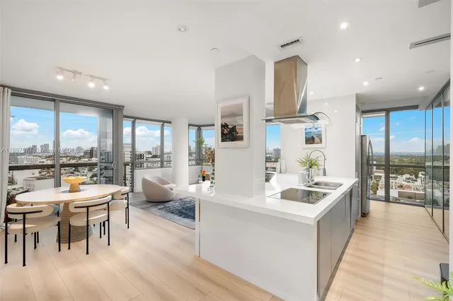 a large dining hall with stainless steel appliances kitchen island granite countertop a refrigerator a sink a stove and a dining table with wooden floor