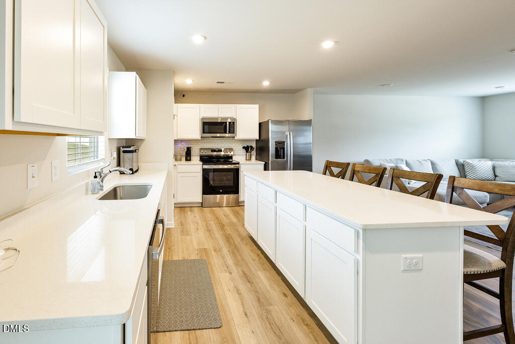 4468 Captain Falls Drive Raleigh, NC 27610 - Photo 5 of 36 a large white kitchen with kitchen island a stove a sink a refrigerator and cabinets