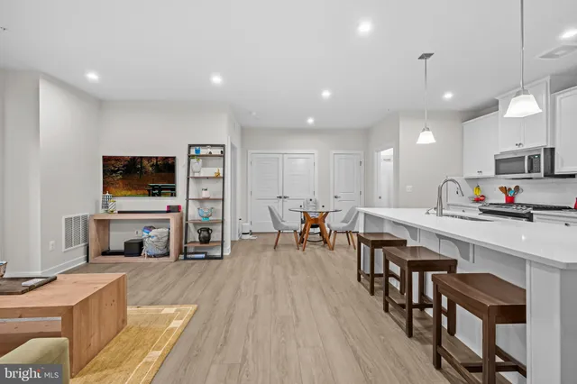 a living room with stainless steel appliances a kitchen island hardwood floor and a sink