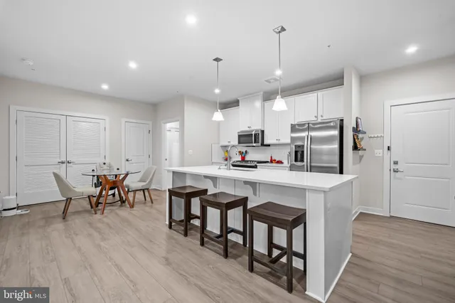 a kitchen with kitchen island granite countertop a dining table chairs refrigerator and cabinets