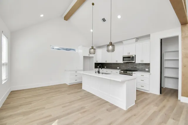 a large kitchen with stainless steel appliances a large counter top a stove a chimney and a wooden floor