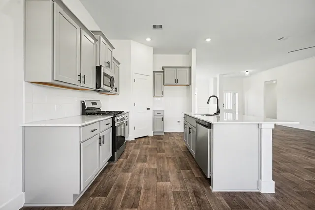 a kitchen with stainless steel appliances a stove top oven a sink a refrigerator white cabinets and wooden floor