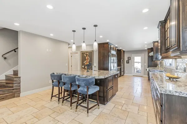 a dining hall with stainless steel appliances kitchen island granite countertop a dining table chairs and a refrigerator