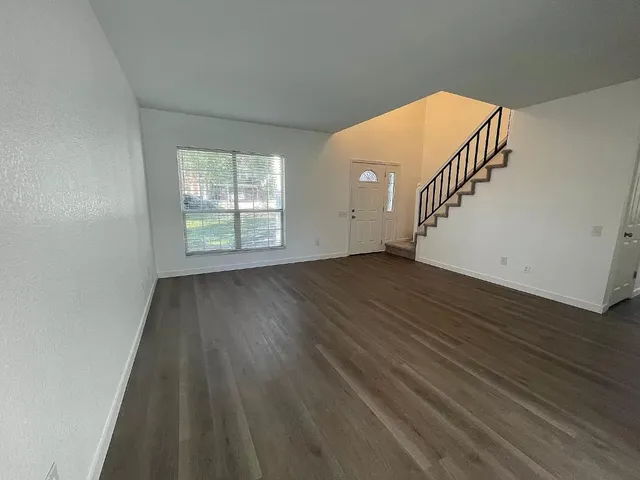 a view of an empty room with wooden floor and stairs