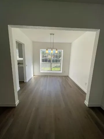 an empty room with wooden floor and kitchen view