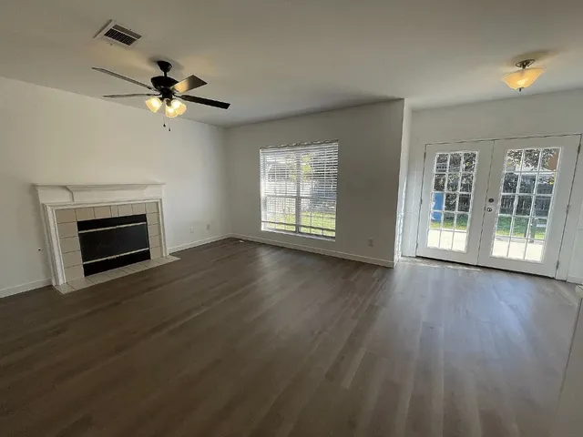 a view of an empty room with wooden floor fireplace and a window