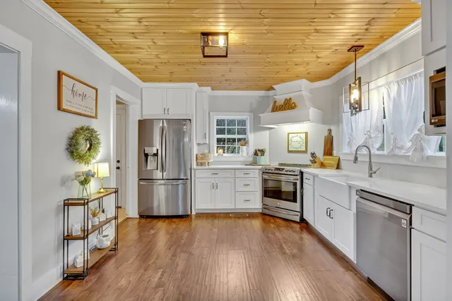 a kitchen with stainless steel appliances a refrigerator a stove top oven a sink dishwasher and white cabinets with wooden floor