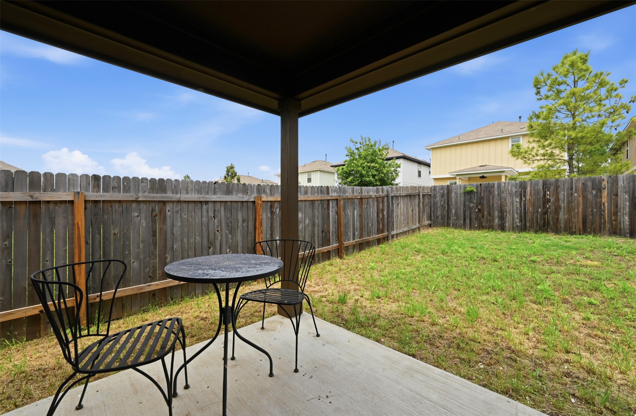303 Limerick Road Buda, TX 78610 - Photo 19 of 23 Covered patio area with concrete flooring, framed by a wooden privacy fence, and featuring a grass lawn