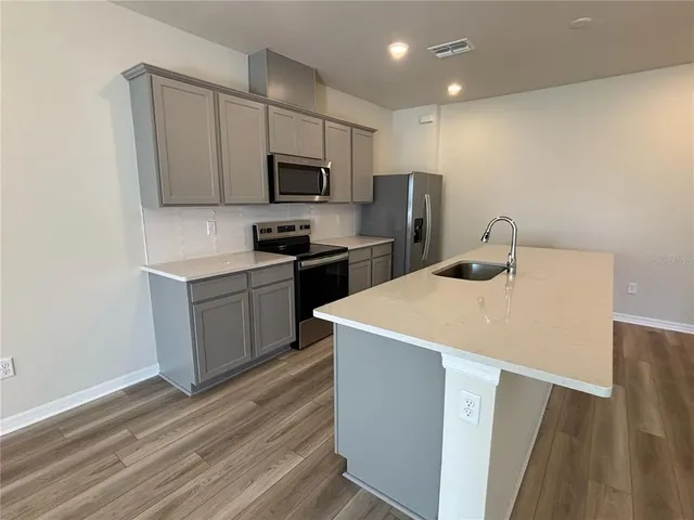 a kitchen with stainless steel appliances a stove top oven a sink a refrigerator white cabinets and wooden floor