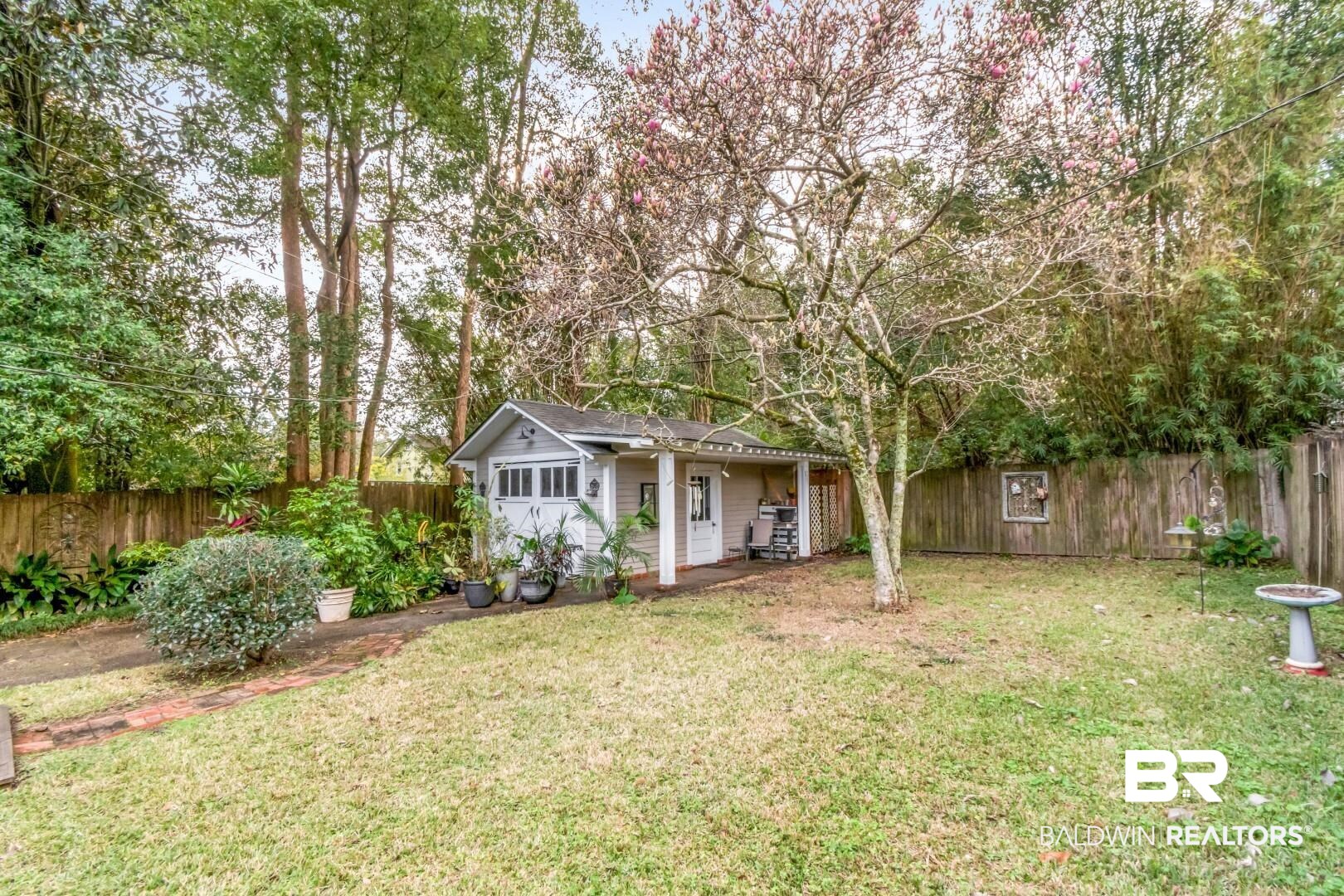 135 Silverwood Street Mobile, AL 36607 - Photo 25 of 32 View of front of house with a fenced backyard, an outdoor structure, a porch, and view of wooded area