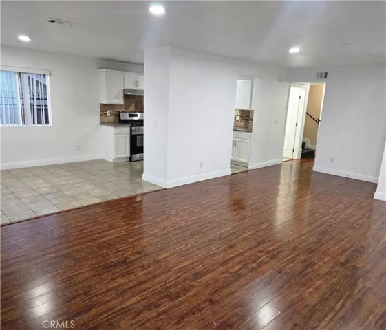 an empty room with wooden floor kitchen view and a window