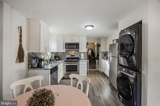 a kitchen with stainless steel appliances a stove a sink dishwasher a refrigerator white cabinets and wooden floor