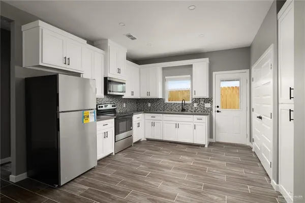 a kitchen with granite countertop a refrigerator oven a sink dishwasher and white cabinets with wooden floor