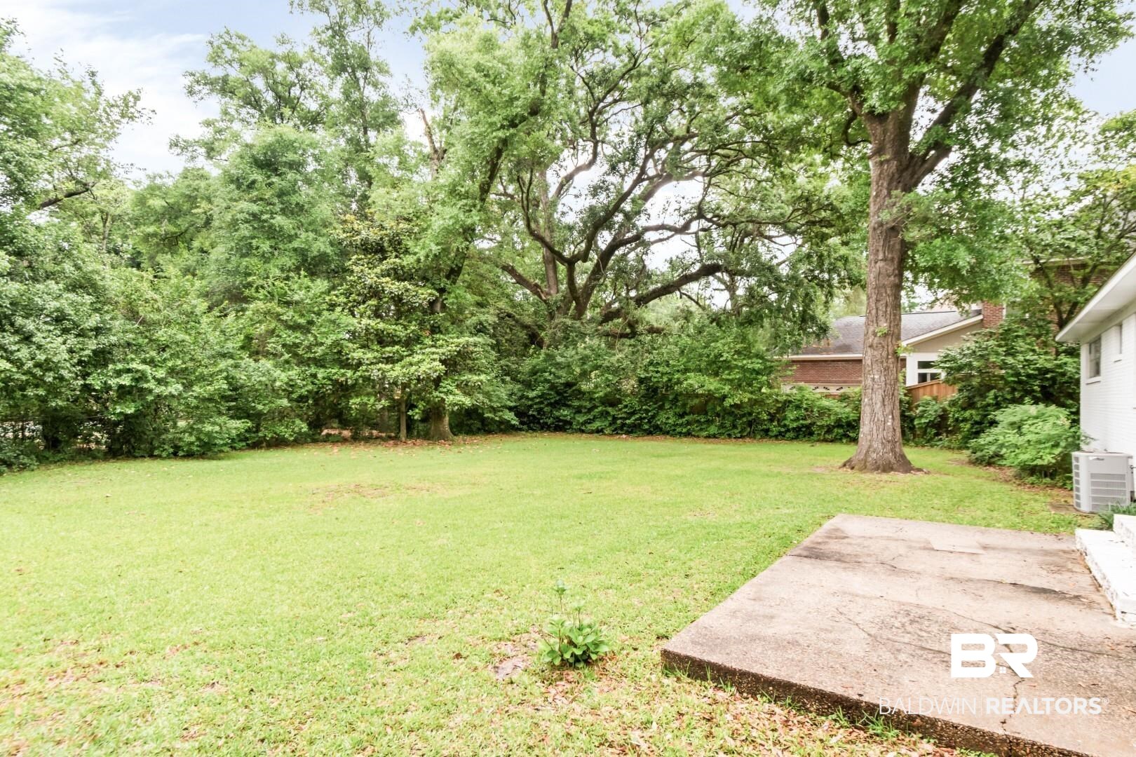 4596 Hawthorne Place Mobile, AL 36608 - Photo 26 of 34 Expansive backyard featuring a large tree, lush green lawn, mature perimeter landscaping, and a concrete patio pad