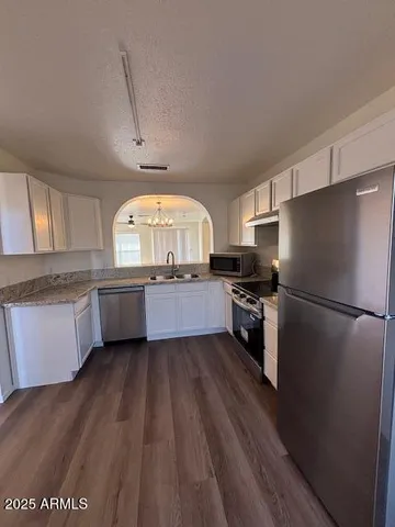 a kitchen with stainless steel appliances granite countertop a sink a stove a refrigerator with white cabinets and wooden floor