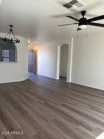 an empty room with wooden floor chandelier fan and windows