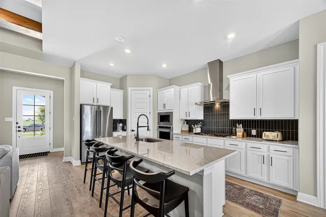 a kitchen with stainless steel appliances kitchen island granite countertop a refrigerator a stove a sink a dining table and chairs with wooden floor