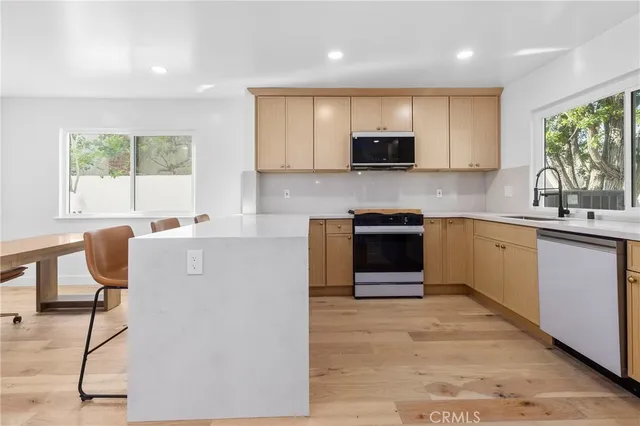 a kitchen with stainless steel appliances granite countertop a stove top oven a sink dishwasher a dining table and chairs with wooden floor