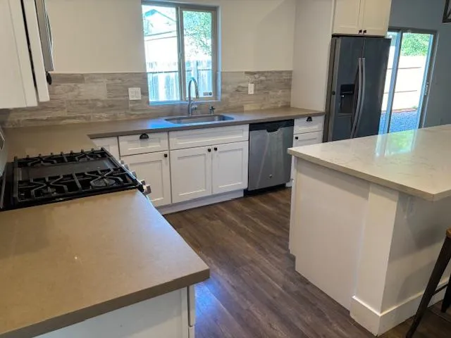 a kitchen with granite countertop a stove a sink dishwasher a refrigerator and wooden floor