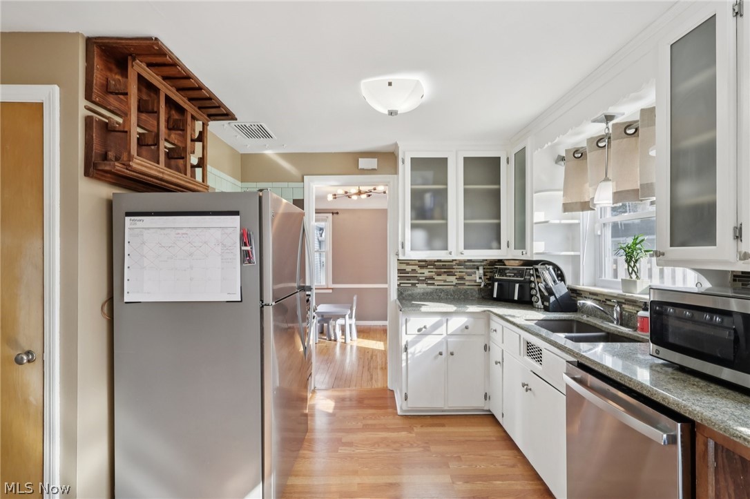 4784 Burger Road Cleveland, OH 44121 - Photo 8 of 27 Kitchen with stainless steel appliances, white cabinets, light wood-style floors, glass insert cabinets, and dark stone counters